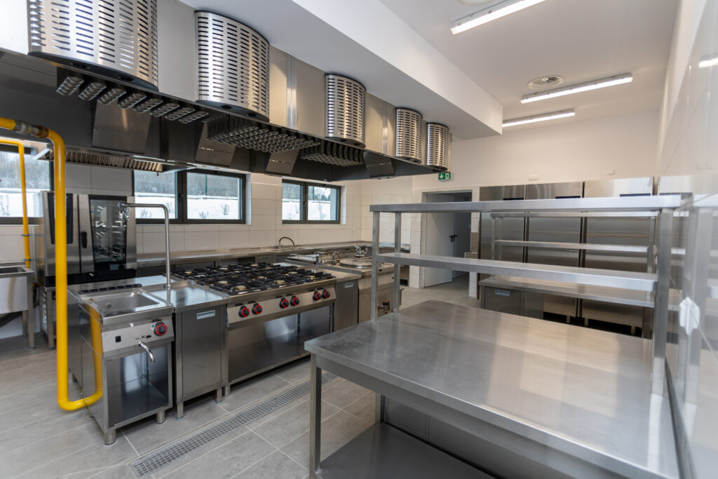 Spacious, well-equipped modern commercial kitchen featuring stainless steel surfaces and appliances.
